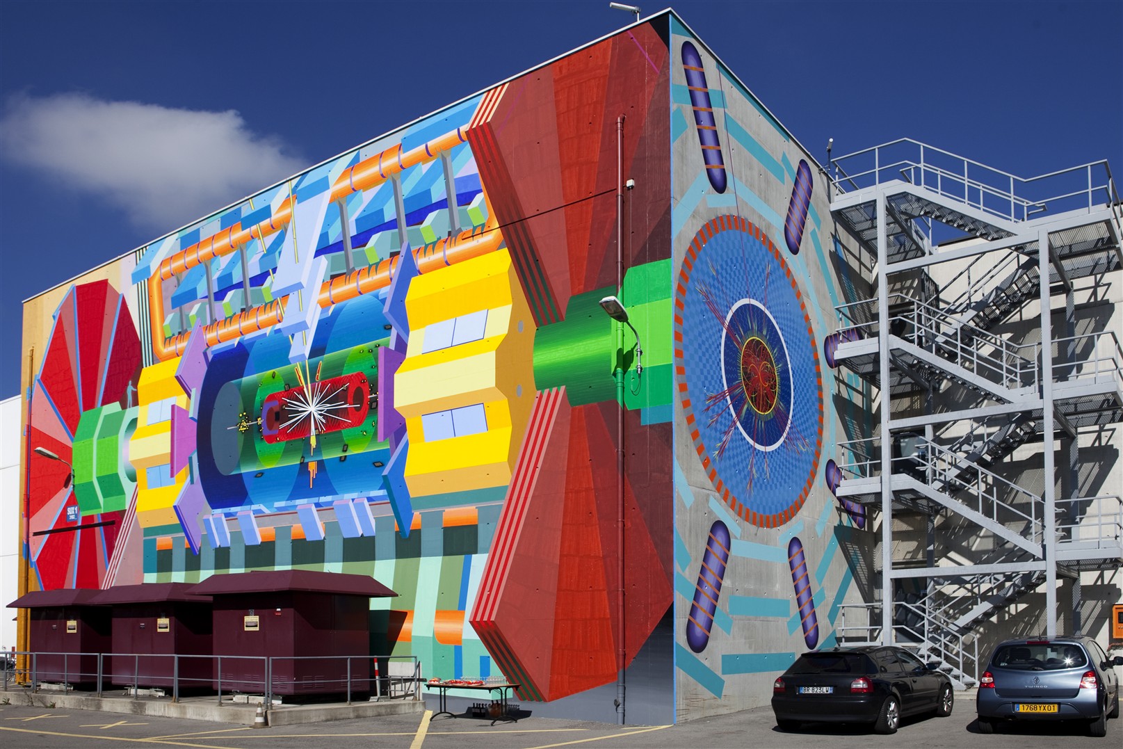 The massive mural of the ATLAS detector at CERN painted by artist Josef Kristofoletti. The mural is located at the ATLAS Experiment site and shows on two perpendicular walls the detector with a collision event superimposed. The event on the large wall shows a simulation of an event that would be recorded in ATLAS if a Higgs boson was produced. The cavern of the ATLAS Experiment with the detector is 100 m directly below the mural. The height of the mural is about 12 m. The actual ATLAS detector is more than twice as big.